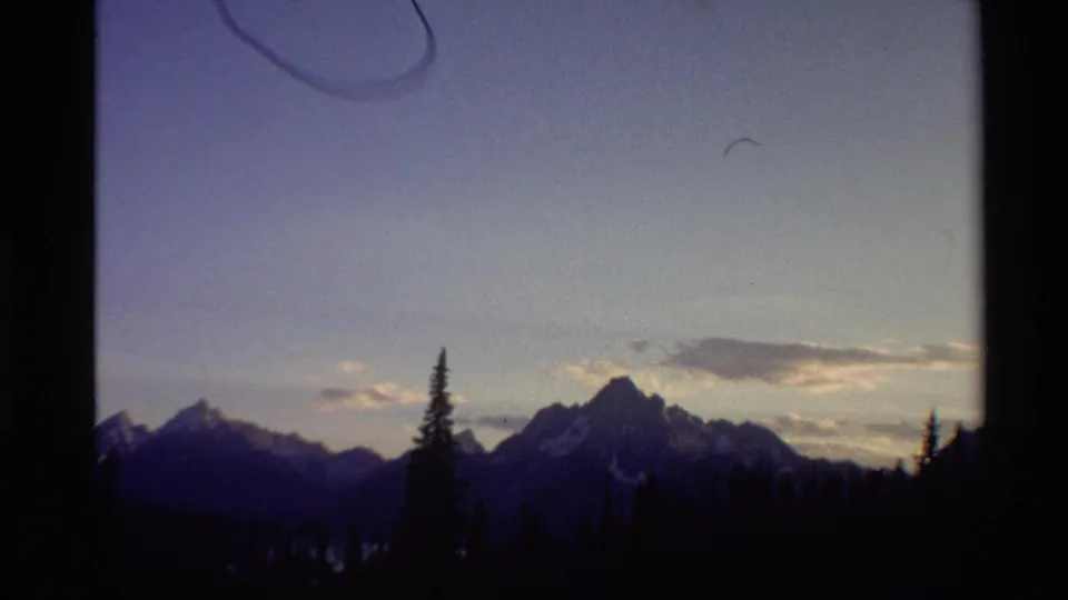 1980 Western U.S. 8mm frame showing distant mountain peaks, tree silhouettes, pale dusk sky, and visible film border artifacts.