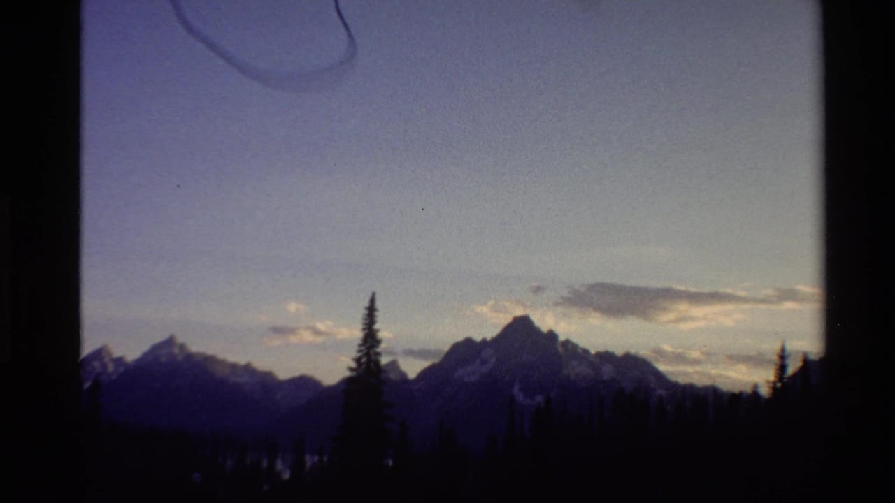 1980 Western U.S. 8mm frame with mountain silhouettes, scattered snow patches, evergreens, and a dimming blue-purple sky.