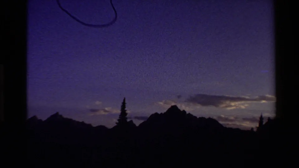 1980 Western U.S. 8mm frame showing the landscape later in the time-lapse, with mountains and evergreens nearly black against a purple sky.