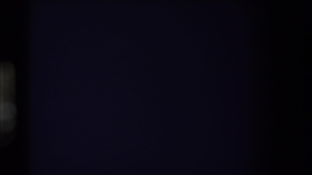 Dark opening frame from an 8mm home movie, with only a faint vertical light shape visible along the left side.
