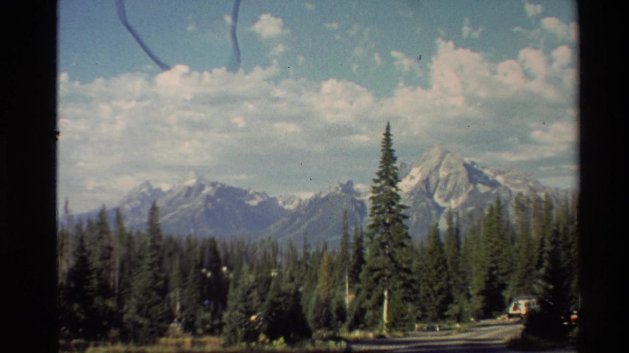 Mountain range behind evergreens with dark frame borders around the view.