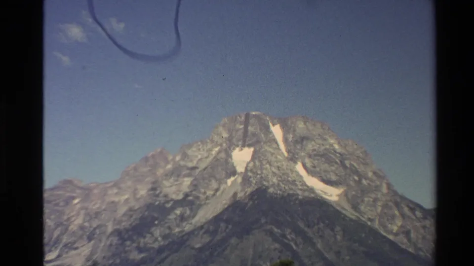 1980 Western U.S. 8mm frame with a closer view of rocky peaks, snow streaks, blue sky, and visible film artifacts.