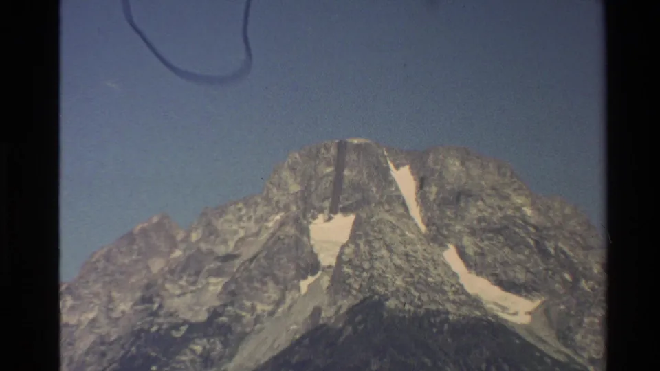1980 Western U.S. 8mm frame showing a tight mountain landscape with snow patches, rocky texture, blue sky, and gate shadowing.
