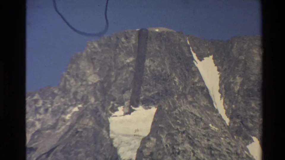 1980 Western USA 8mm frame focused on a rocky mountain face, showing snow accumulation in steep gullies and visible film wear.