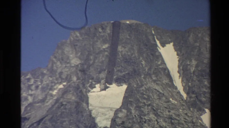 1980 Western USA 8mm close view of the gray mountain peak, with bright snow patches, blue sky, and darkened film edges.