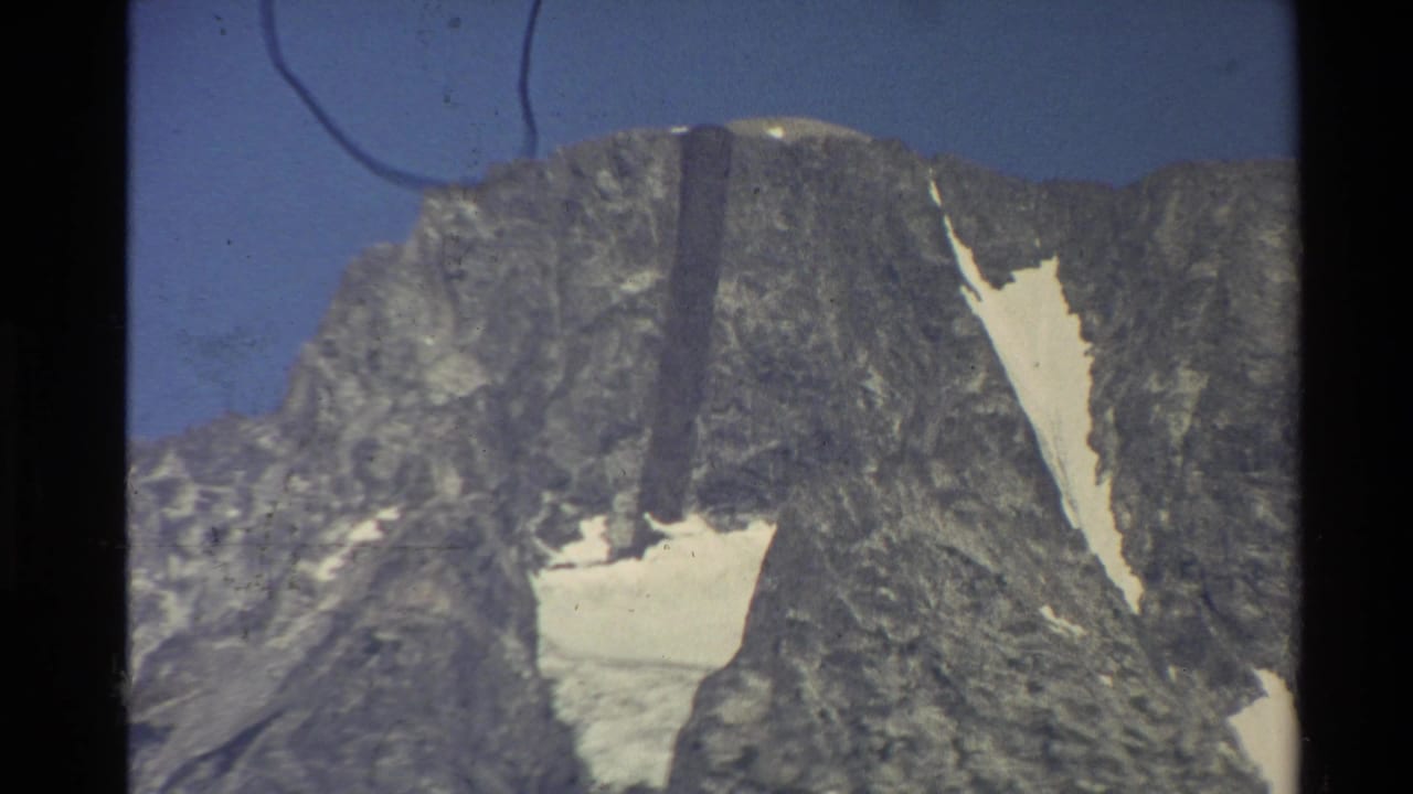 Similar view of a rocky snow-patched mountain peak beneath clear blue sky.