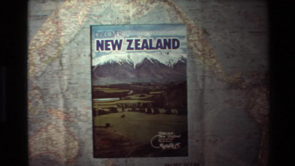 Final frame of the static 1981 8mm shot, with the New Zealand travel book on the printed map and soft archival color fading.