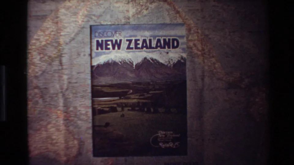 1981 8mm frame showing a Discover New Zealand travel brochure projected against a map-like background.