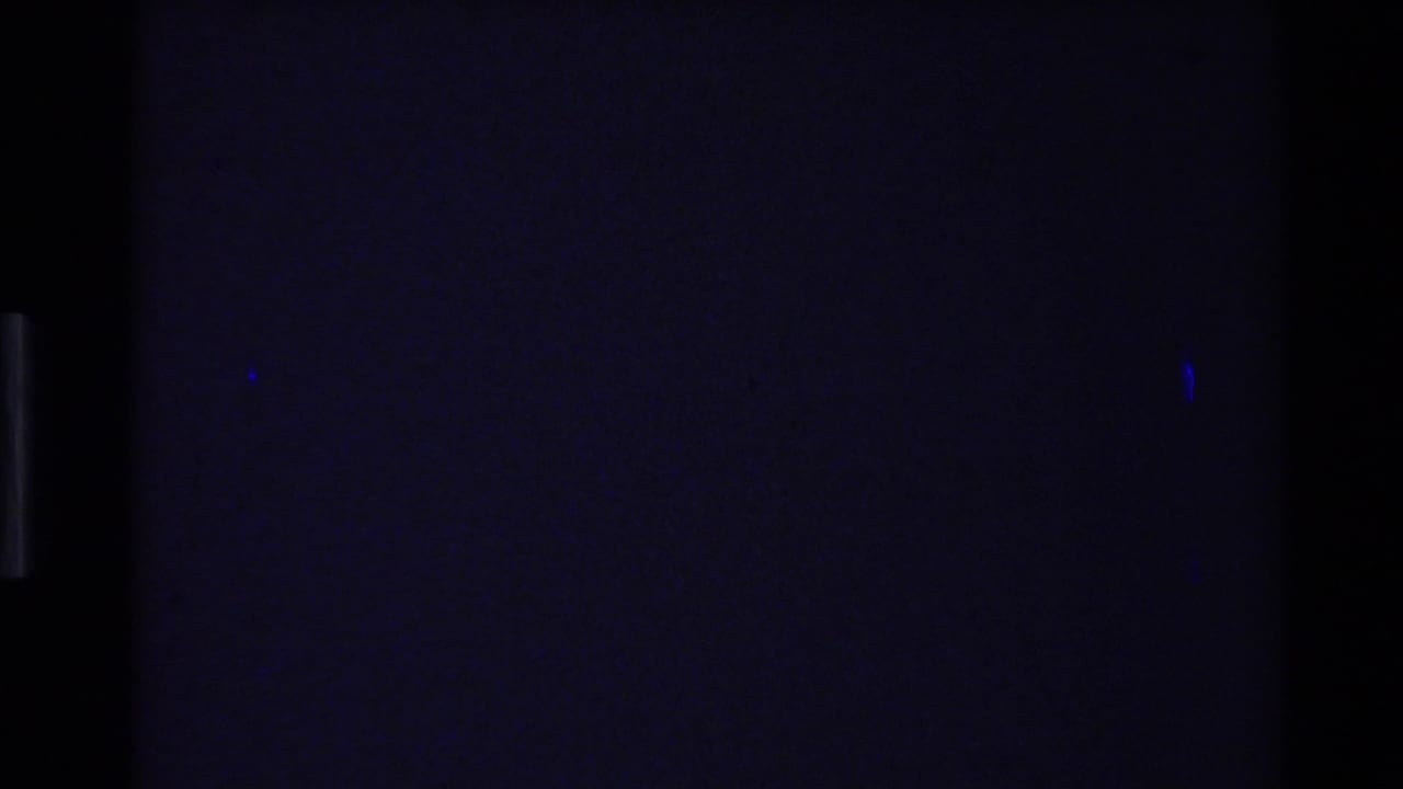 Mostly dark projected frame with faint blue marks and film borders.