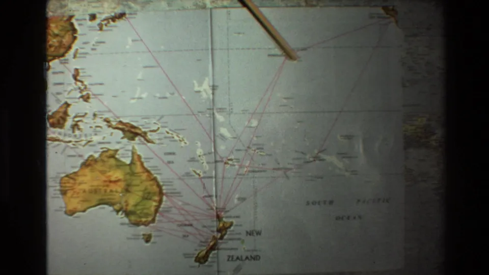 1981 8mm frame showing a wooden pointer over a South Pacific map marked with routes from Australia and New Zealand.