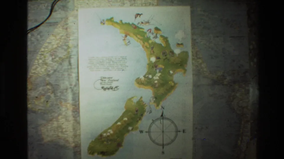 The frame holds on the illustrated New Zealand map, with island shapes, small drawings, and a compass rose visible on 8mm film.