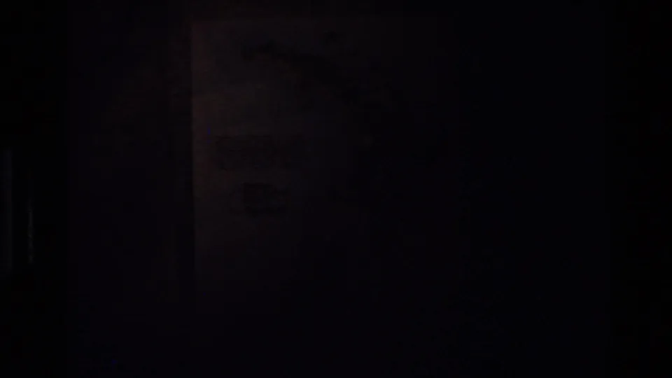 A mostly dark transitional frame where a faint map or wall detail is barely visible in the 8mm scan.