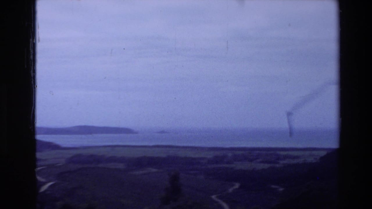 Coastal hills and calm water under a cloudy sky with dark film borders.
