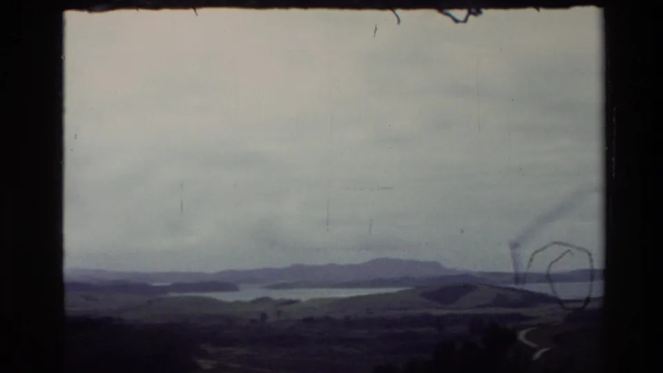 Faded 1981 New Zealand 8mm view of a low coastline, water, distant hills, and visible film marks.