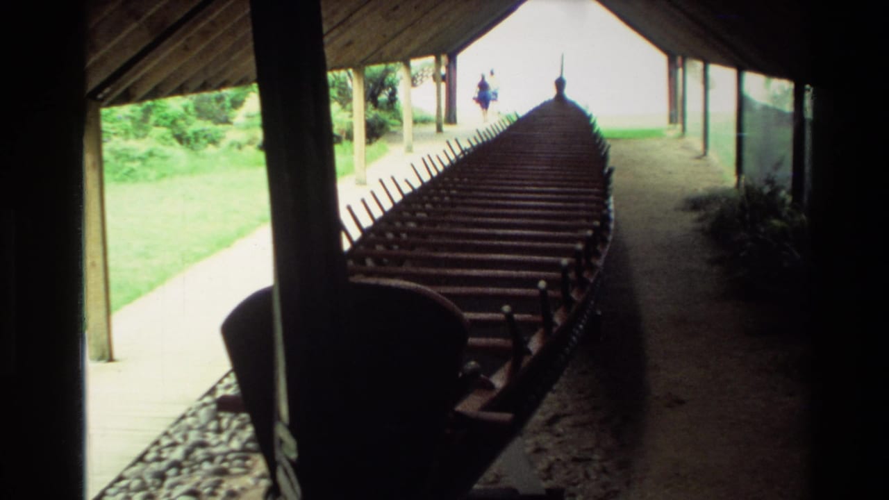 View down the length of a wooden waka with many cross seats under a shelter.