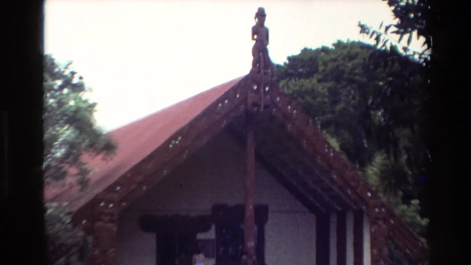 Closer 1981 New Zealand view of the meeting-house gable, showing carved timber details, red roofing and surrounding foliage.