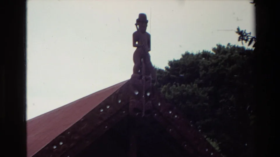 Zoomed 8mm frame from New Zealand in 1981 focusing on the carved figure at the meeting-house roof apex.