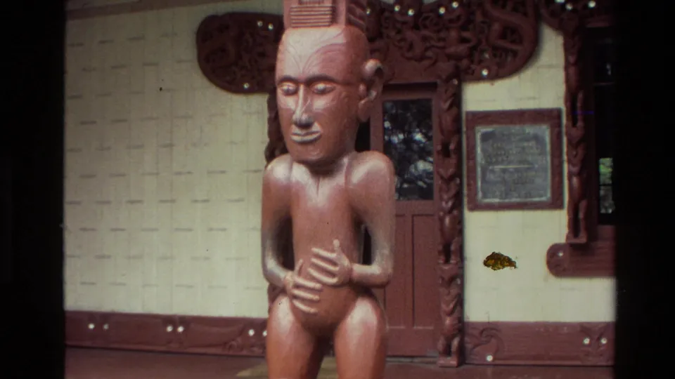 1981 New Zealand 8mm close view of a carved seated figure with hands over the abdomen, set beside a decorated doorway.