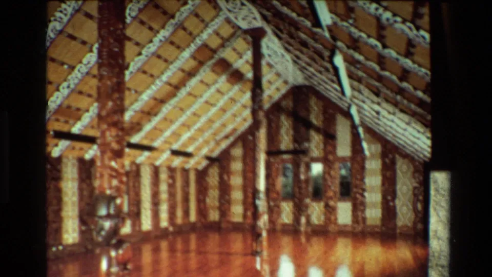 1981 New Zealand frame showing an ornate meeting house interior with carved posts, patterned rafters, and warm 8mm color.