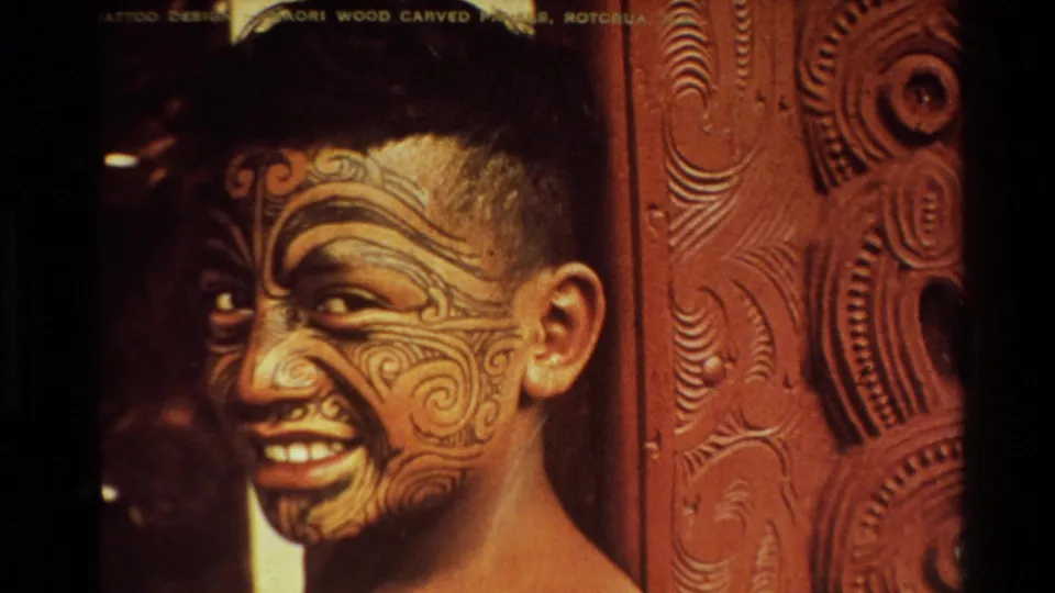 1981 New Zealand 8mm close-up of a smiling Maori man with facial moko beside carved wooden interior panels.