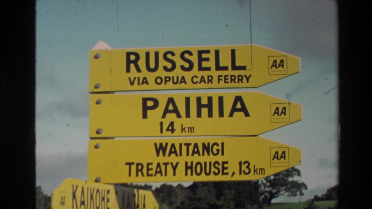 New Zealand 1981 travel footage frame with yellow AA directional signs, including Russell via Opua Car Ferry and Paihia at 14 km.