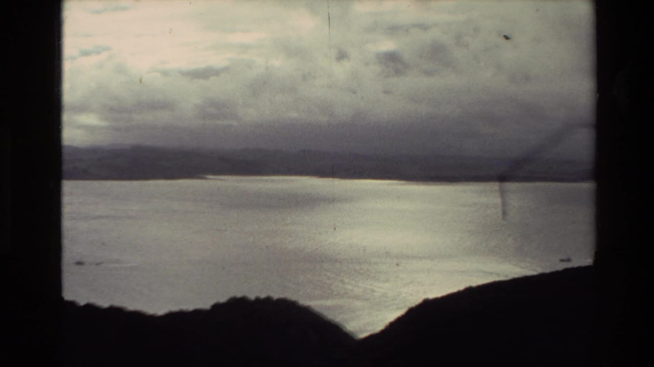 Wide coastal view with water, dark hills, distant land, and heavy cloud cover.