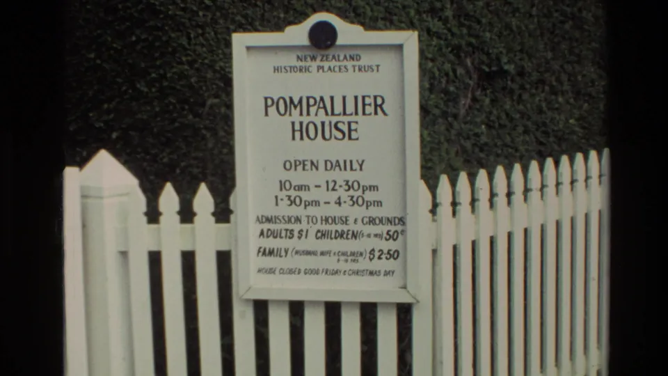 1981 New Zealand 8mm frame of the Pompallier House sign for visitors, framed by a white picket fence and greenery.