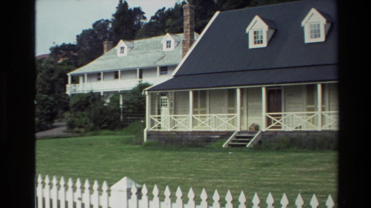 1981 New Zealand 8mm frame showing a white picket fence, green lawn, and colonial-style house near Christ Church Russell.