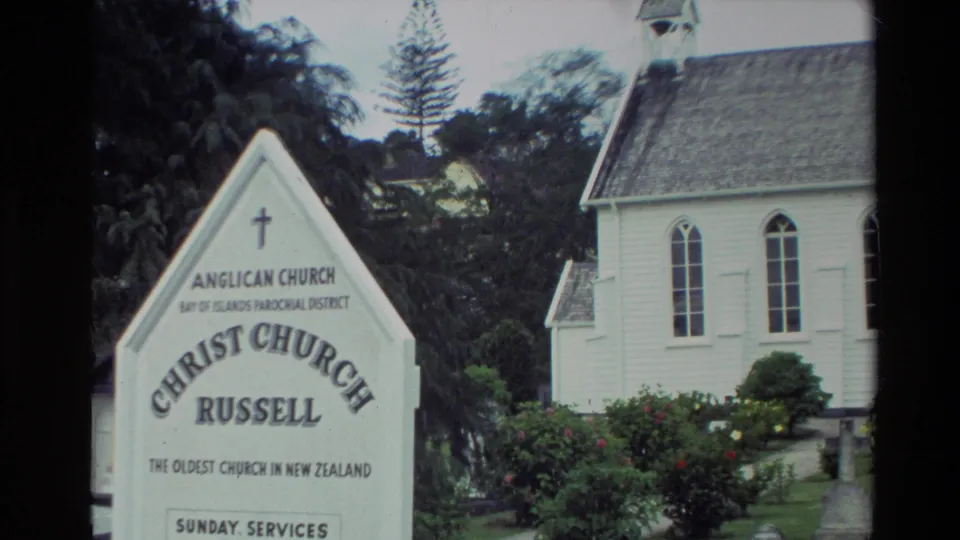1981 New Zealand frame showing the Christ Church Russell sign with the white timber church, Gothic-style windows, shrubs, and bell tower behind it.