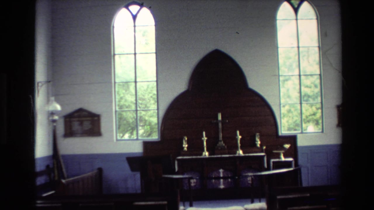 1981 New Zealand 8mm frame showing a small church interior with tall arched windows, a dark wooden altar screen, a cross, and candlesticks.