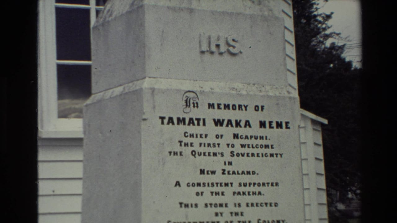 Visitor-shot 8mm view of the Tamati Waka Nene memorial inscription in New Zealand, with white siding and a window behind it.