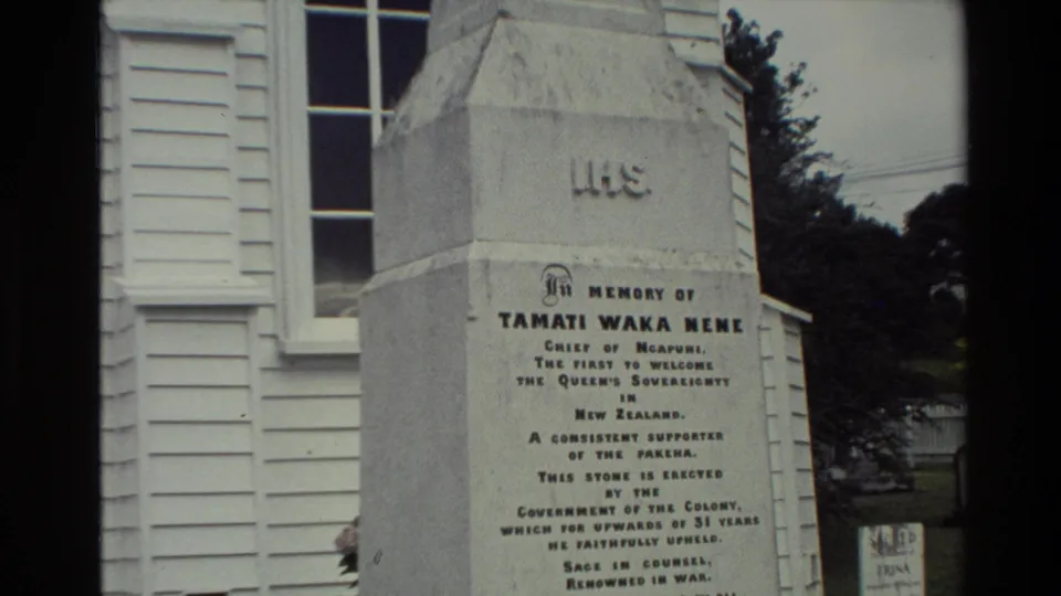 Wider 1981 New Zealand 8mm view of the Tamati Waka Nene obelisk, showing more of the building, trees, and surrounding grounds.