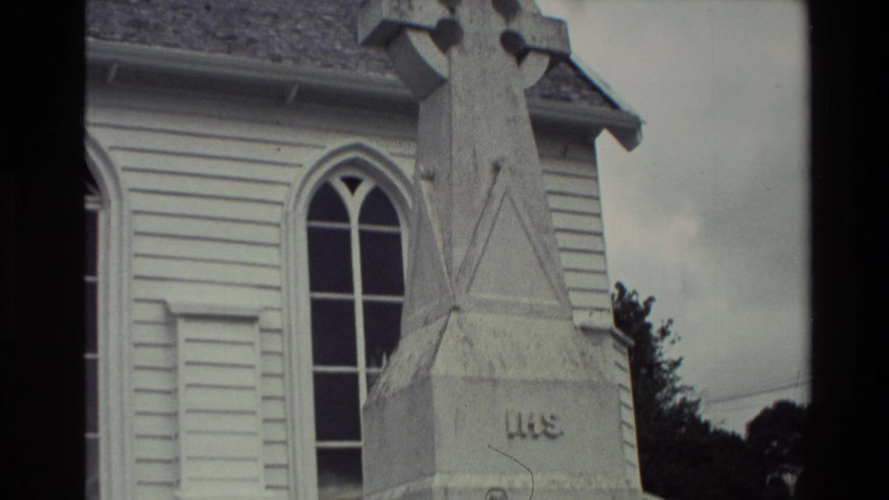 Upper section of a stone cross monument beside a church window and roofline.