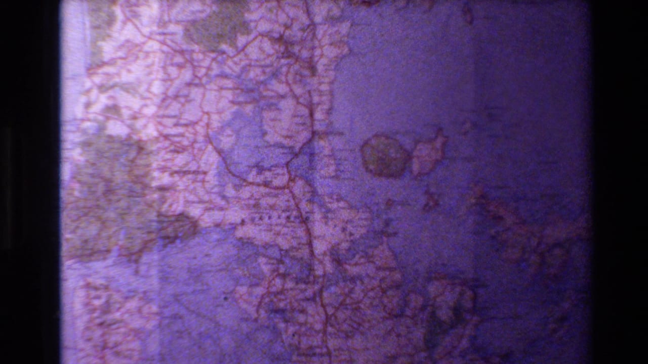 1981 8mm frame showing a New Zealand roadmap with blue water, red road lines, printed labels, and a purple aged-film cast.