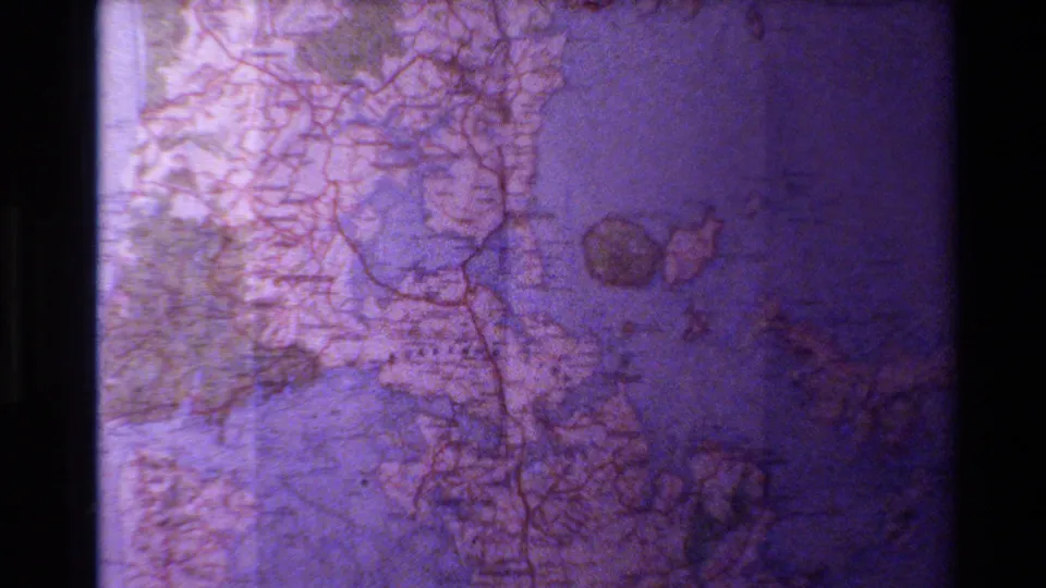 1981 8mm frame showing a New Zealand roadmap with blue water, red road lines, printed labels, and a purple aged-film cast.