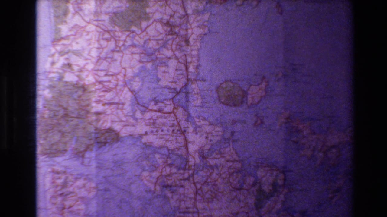 The zoom continues over a New Zealand map, with roads, coastal shapes, and small printed place names softened by 8mm grain.