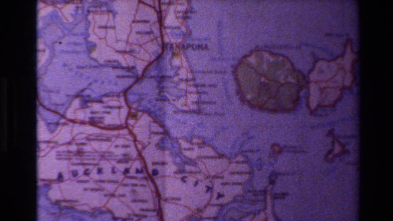 1981 New Zealand home-movie frame of a printed Auckland-area map, with purple cast, coastline markings, and visible film edges.
