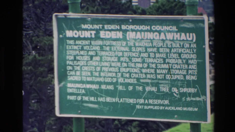 Close handheld view of the Mount Eden Maungawhau sign, with explanatory text visible but partly soft.