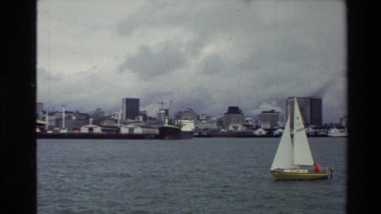 Small sailboat on an urban bay with a distant skyline under cloudy skies.