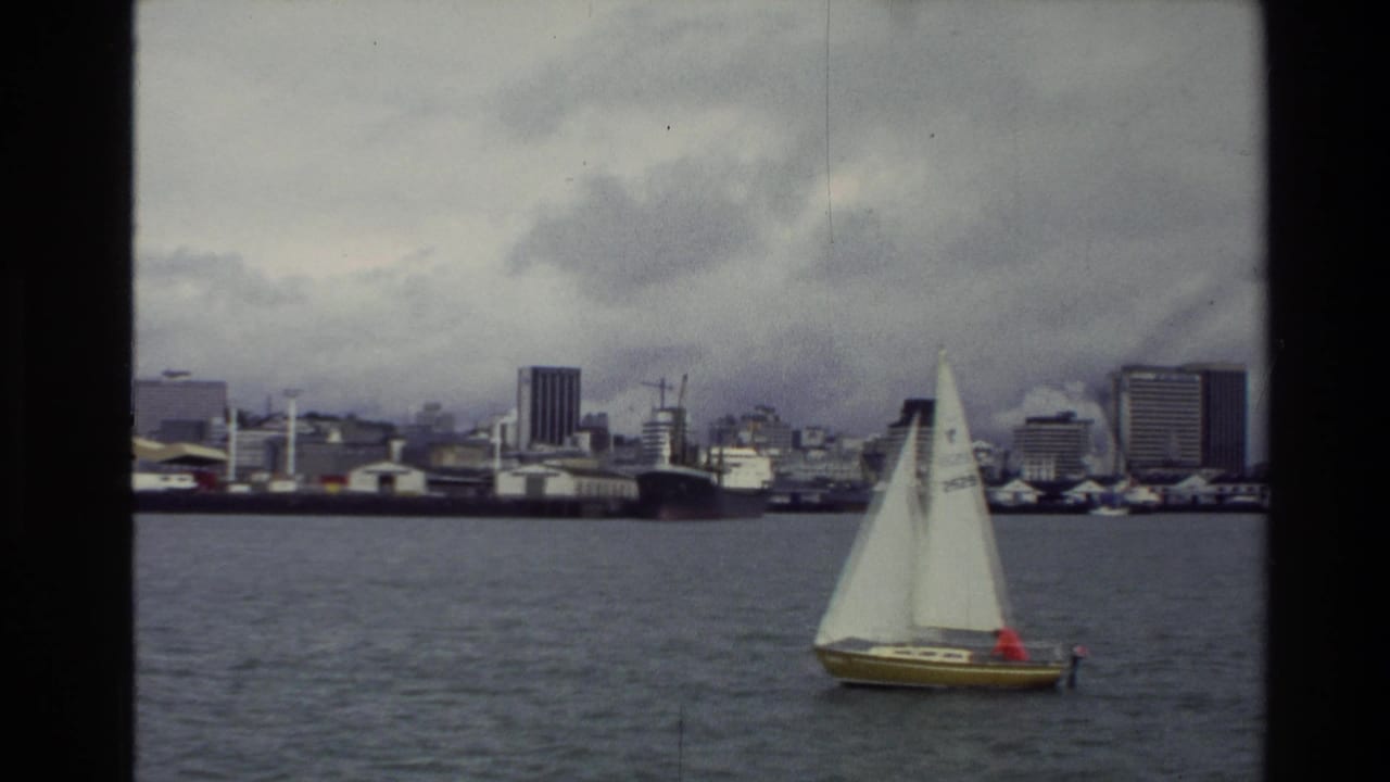 Sailboat near the right side of the frame with city buildings across the water.