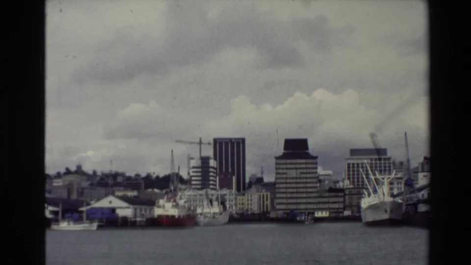 The final frame shifts to the New Zealand waterfront, showing moored vessels, cranes, and mid-rise buildings across the bay in 1981 footage.