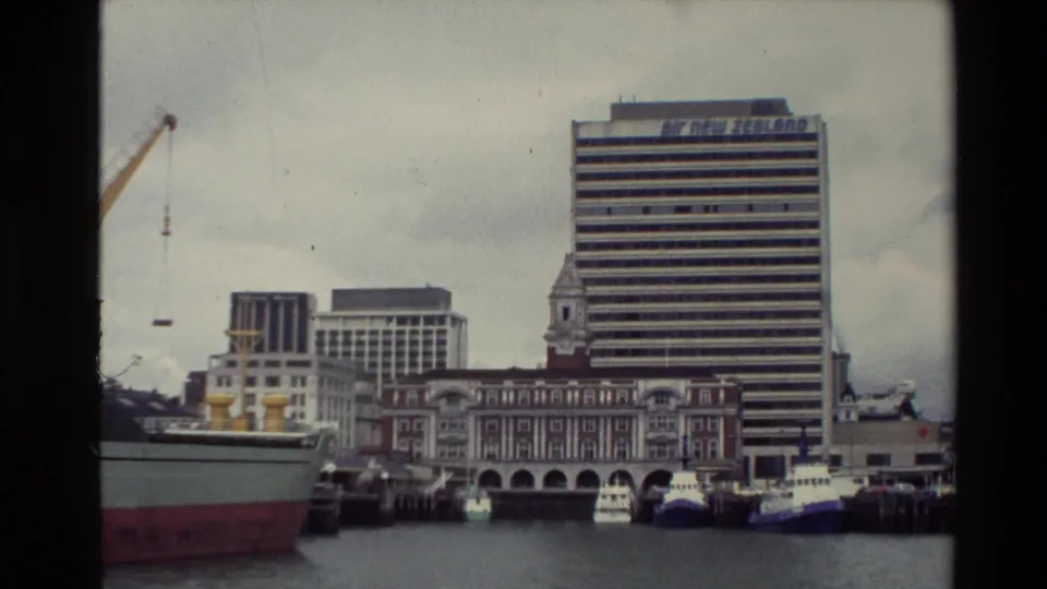 1981 New Zealand waterfront view with docked ships, cranes, older buildings, and a tall office block carrying Air New Zealand signage.