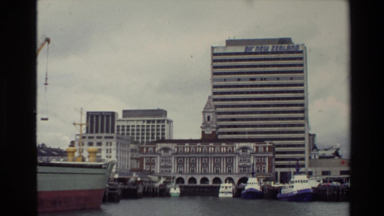 Harbor view with cargo vessel, small boats, older waterfront building, and Air New Zealand office tower.