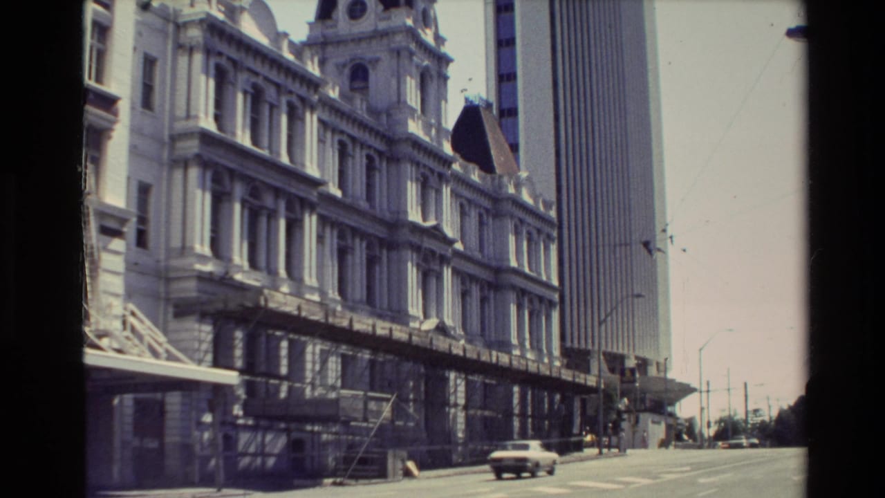 1981 New Zealand street view showing an ornate older building, scaffolding, a tall modern tower, and classic cars passing below.
