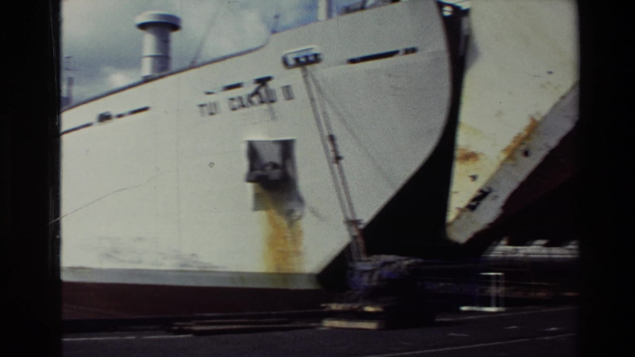 1981 New Zealand 8mm frame showing the bow and forward hull of a white cargo ship near another docked vessel.