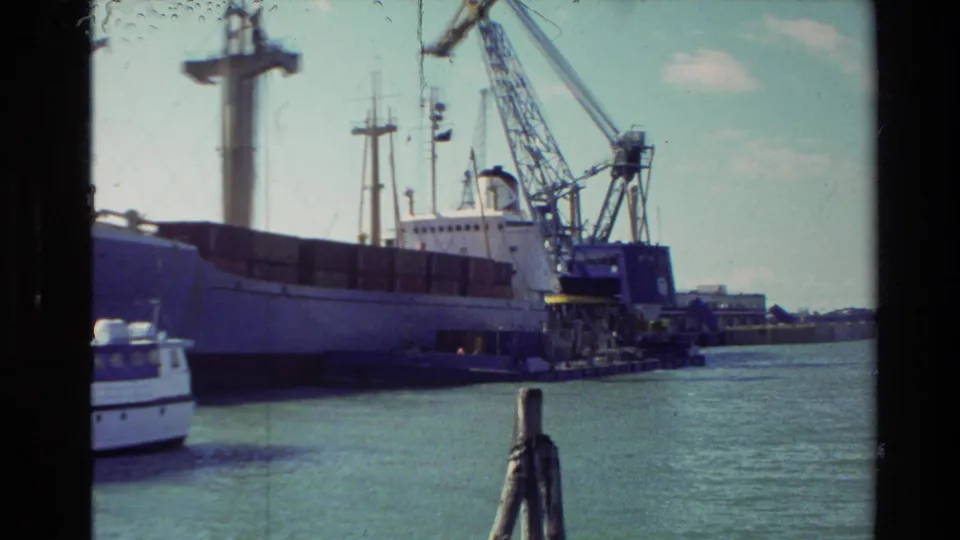 1981 New Zealand 8mm frame showing a docked cargo ship with harbor cranes and a small boat near the waterline.
