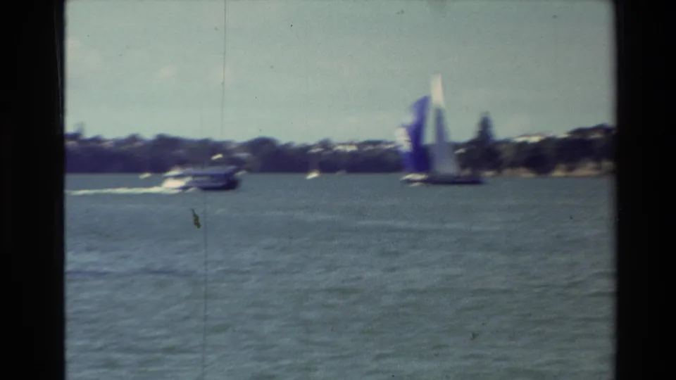Soft 1981 New Zealand 8mm frame showing a blue-and-white sailboat near a small motor boat on a lagoon or harbor.