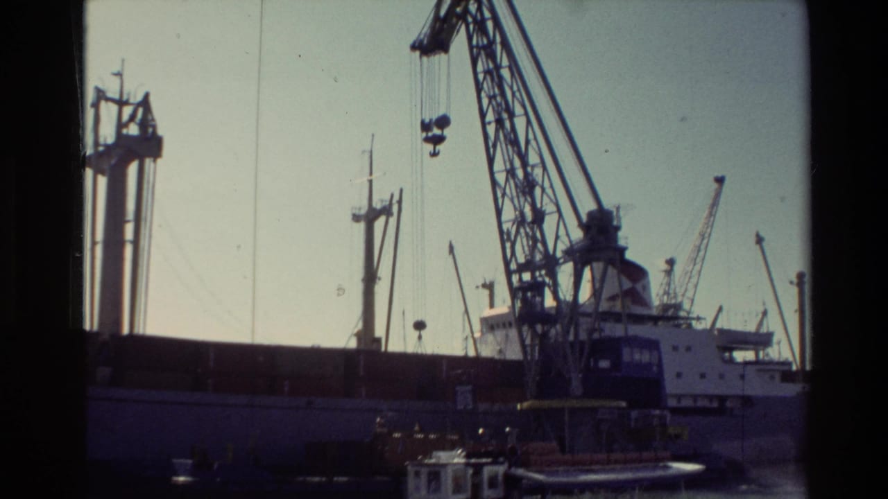 1981 New Zealand port scene showing cranes over a docked barge, with a tugboat partly cropped in the foreground.