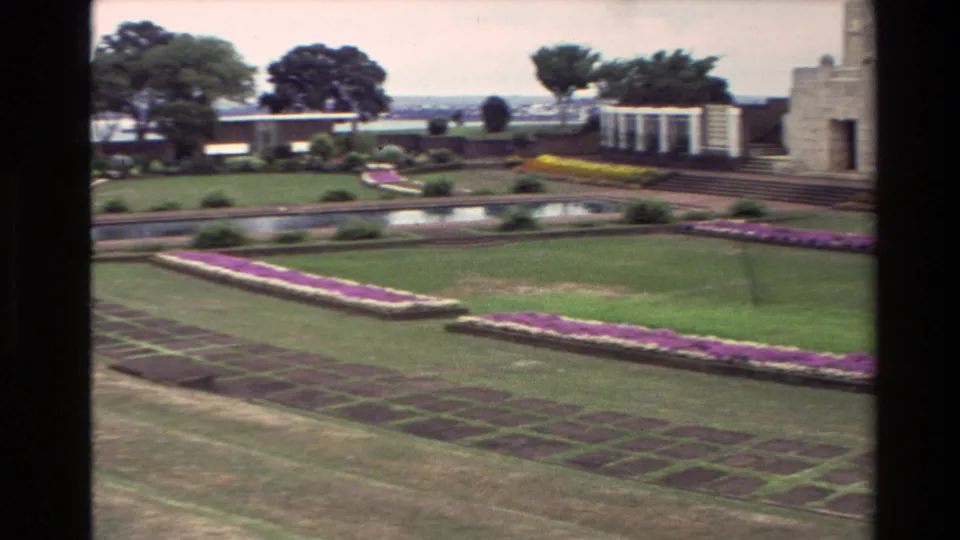 1981 New Zealand 8mm frame showing formal flower beds, a reflecting pool, lawns, trees, and part of a stone memorial structure.