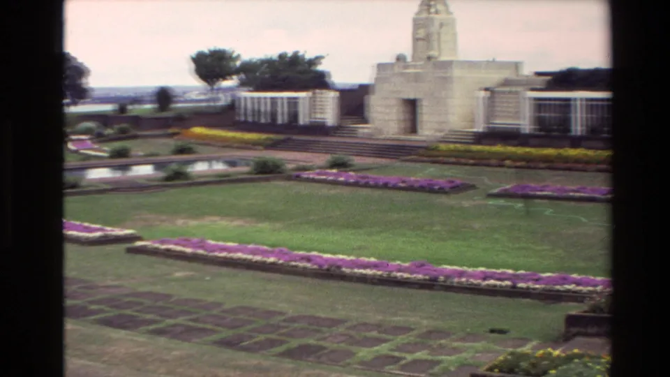 1981 New Zealand 8mm frame with a stone memorial building, formal lawns, purple flower borders, a reflecting pool, trees, and distant water.